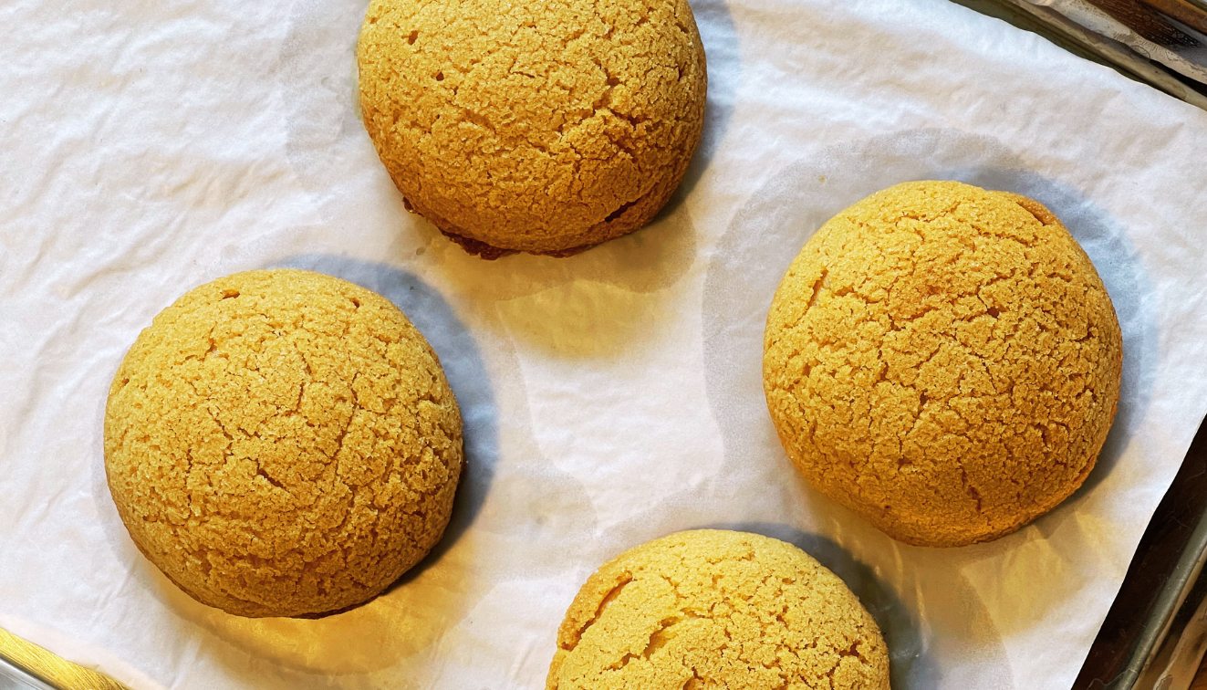 Four round, golden-brown cookies with a cracked surface sit on parchment paper on a baking tray.