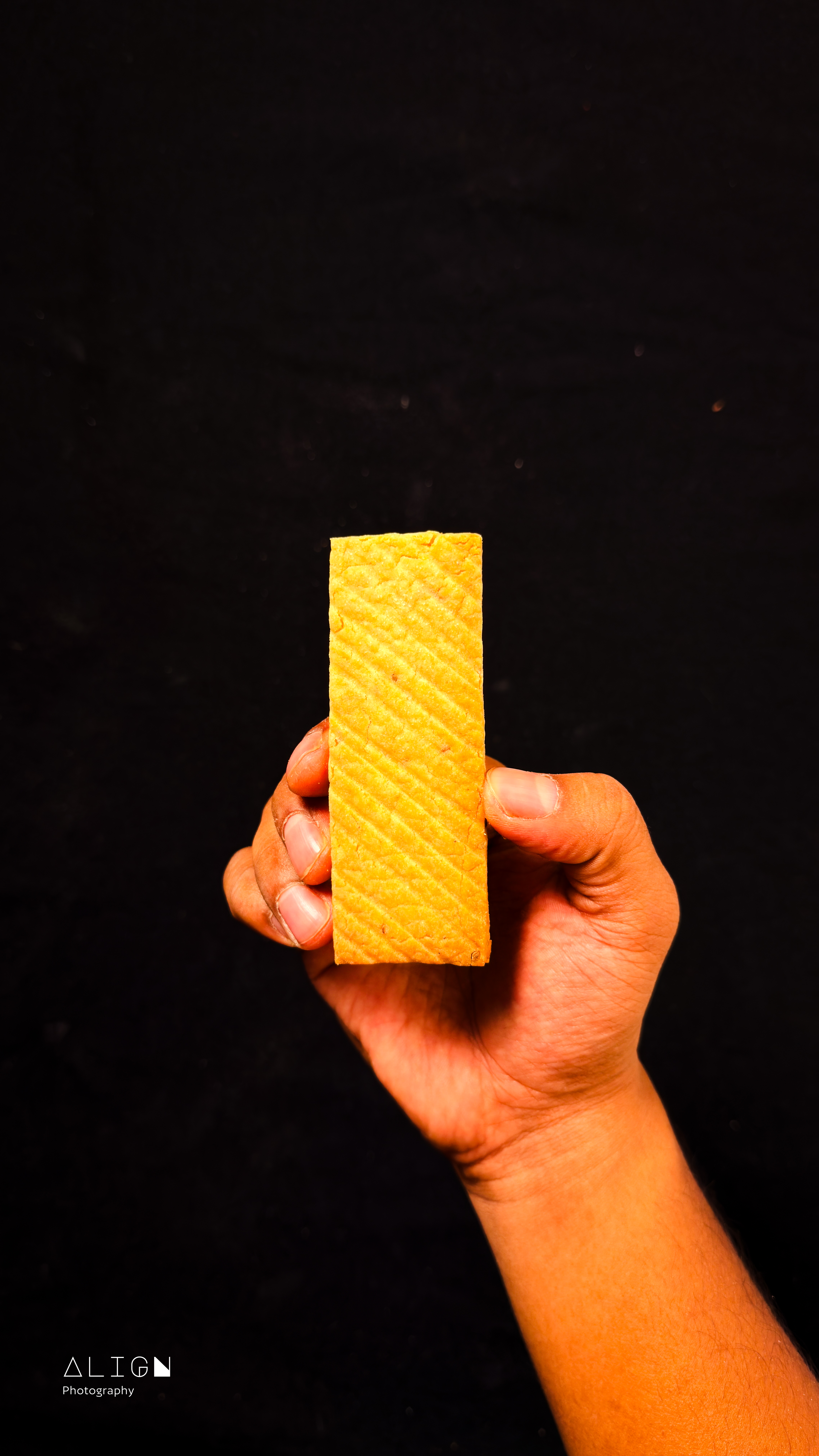 A hand holding a rectangular wafer biscuit against a plain black background.